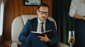 Confident middle-aged businessman working and relaxing during a business trip, writing in a notebook then drinking champagne while traveling in the first class of a private jet - Powered by Shutterstock - Get 15% off with code: PIKWIZARD15