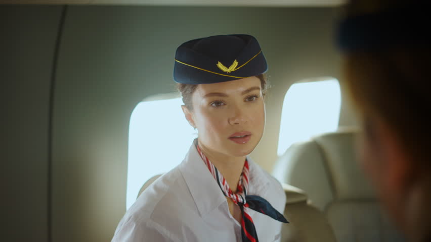 Beautiful flight attendant in uniform smiling and talking to a passenger inside the cabin of a commercial aircraft, providing excellent customer service during the flight for a pleasant journey