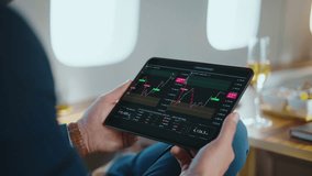 Unrecognized financial analyst holding a foldable tablet while monitoring real-time stock market data. Cryptocurrency exchange rates. And investment charts during a luxurious flight on a private jet - Powered by Shutterstock - Get 15% off with code: PIKWIZARD15