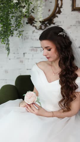 Young bride with brunette hairstyle sitting on couch in photo studio. Gorgeous modern girl on a light isolated background in the studio. 