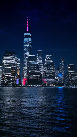 Beautiful dazzling skyscrapers at the waterfront of New York, USA. Metropolis skyline at night from the boat travelling by the river. Vertical video.