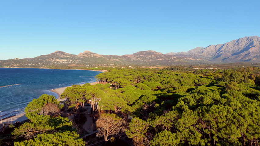 Aerial sunrise over peaceful nature scene, morning light highlights serene beach and mountain landscape. Corsica. France.