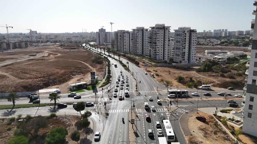 Aerial view of Ashkelon showing busy traffic, residential buildings, and the scenic seaside promenade. Dynamic urban coastline scene with cars in motion and modern city architecture.