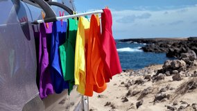 Colorful t shirts forming the LGBT rainbow pride flag hanging from a car rack, waving in the wind with a scenic ocean view. Slow motion video representing freedom, diversity, and love - Powered by Shutterstock - Get 15% off with code: PIKWIZARD15