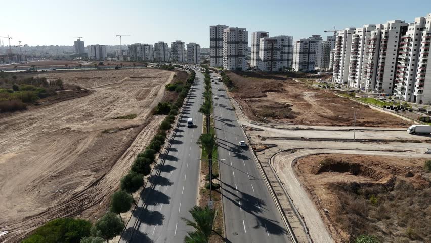 Aerial view of Ashkelon showing busy traffic, residential buildings, and the scenic seaside promenade. Dynamic urban coastline scene with cars in motion and modern city architecture.