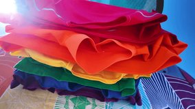 Colorful t shirts arranged in the colors of the pride flag gently waving in the wind against a bright blue sky, symbolizing LGBTQ plus community rights, love, and freedom on a sunny day - Powered by Shutterstock - Get 15% off with code: PIKWIZARD15