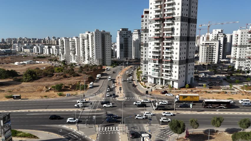 Aerial view of Ashkelon showing busy traffic, residential buildings, and the scenic seaside promenade. Dynamic urban coastline scene with cars in motion and modern city architecture.