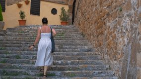 Woman climbing stone stairs in an ancient italian village. Woman in a white summer dress walking up an old stone staircase in a picturesque medieval european town, exploring the historic alleyways - Powered by Shutterstock - Get 15% off with code: PIKWIZARD15