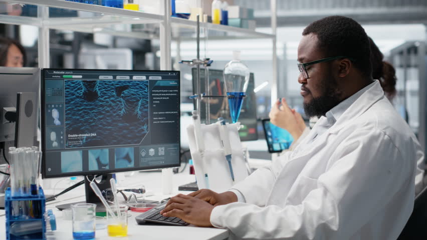 Portrait of smiling laboratory scientist using computer monitor, processing DNA patient data for clinical research. Cheerful african american lab worker looking at analysis diagnostics on PC, camera B - Powered by Shutterstock - Get 15% off with code: PIKWIZARD15