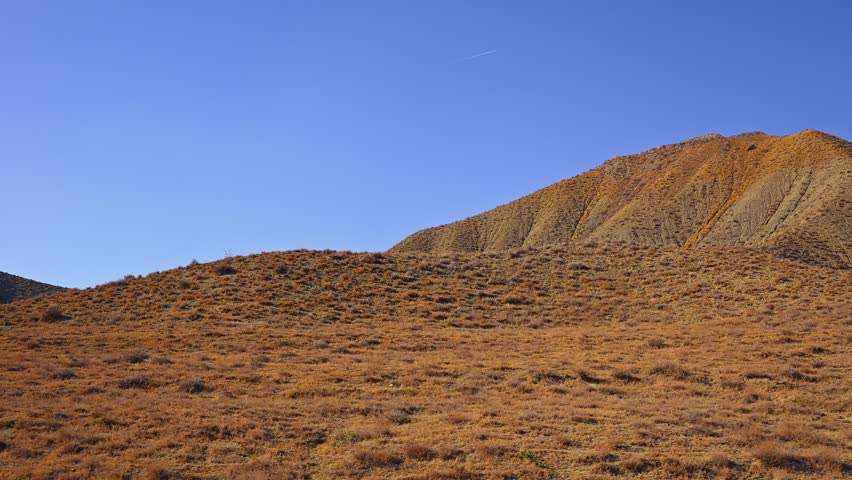 Aerial view large hill with a blue sky in the background. The hill is covered in dry grass and dirt