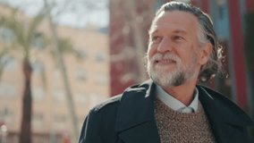 Portrait of a happy senior man with grey hair and beard smiling and looking around a city street on a sunny day. - Powered by Shutterstock - Get 15% off with code: PIKWIZARD15
