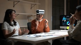Three people are sitting at a table with a computer monitor in front of them. One of the women is wearing a virtual reality headset. Scene is lighthearted and fun - Powered by Shutterstock - Get 15% off with code: PIKWIZARD15