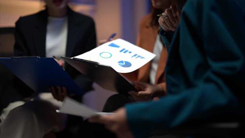 Three women are sitting together and looking at some papers. They are discussing something important. Scene is serious and focused