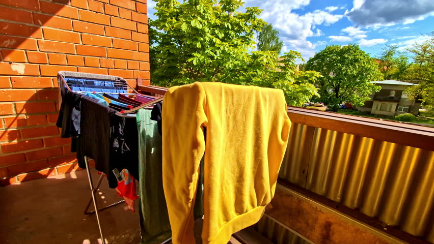 Yellow Sweatshirt Drying On Balcony amongst other Clothes With Trees And Blue Sky In Background
