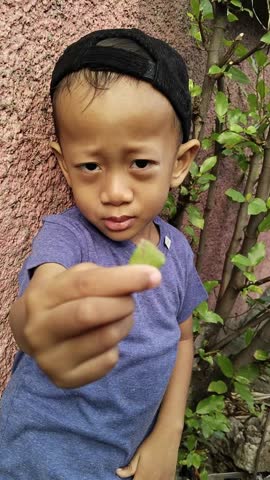 Asian boy wearing a black hat showing a picked leaf to the camera