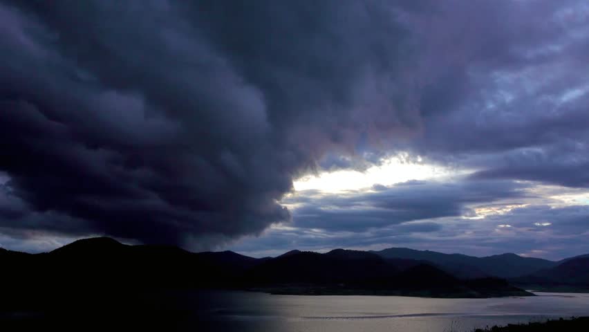 Dramatic storm clouds over a dark lake with mountains in the distance scenery