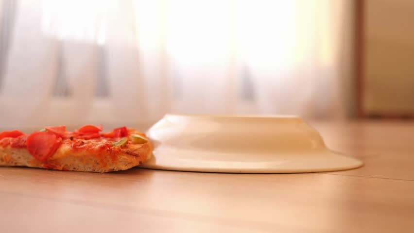 Slice of pizza falling on a wooden floor, messy home 