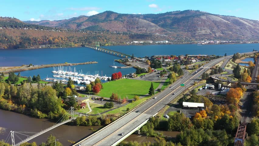 4K aerial drone footage of Hood River Bridge in Oregon, showing I-84 highway traffic,  marina with boats, and city area surrounded by fall colors along the Columbia River in the Pacific Northwest