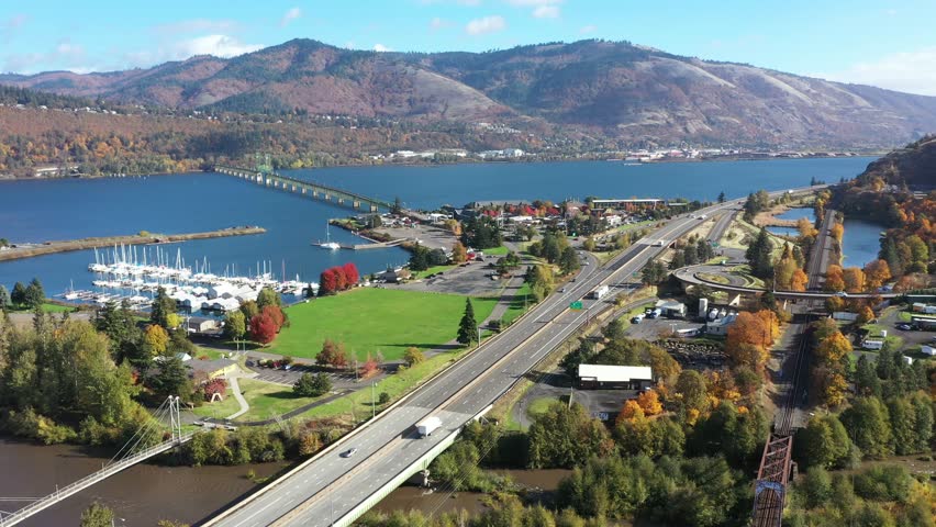 4K aerial drone footage of Hood River Bridge in Oregon, showing I-84 highway traffic,  marina with boats, and city area surrounded by fall colors along the Columbia River in the Pacific Northwest