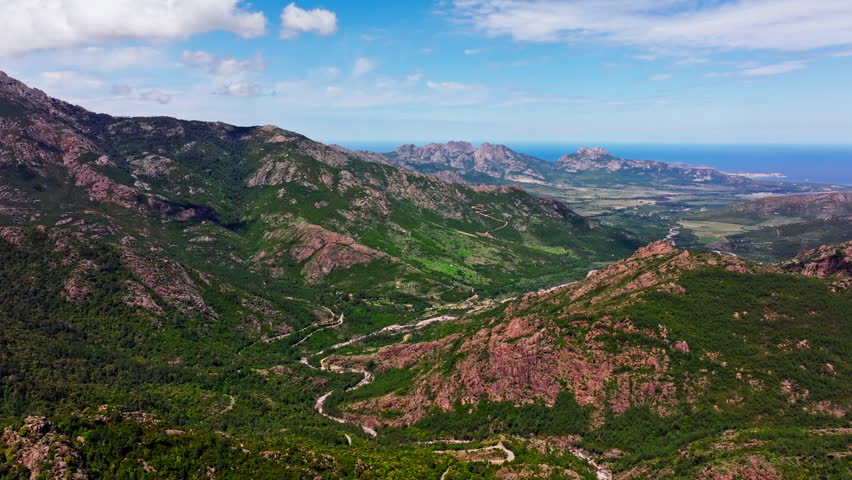 Aerial drone view over the mountainous landscape of Corsica. High view of green rugged landmark and the sea in the distance.