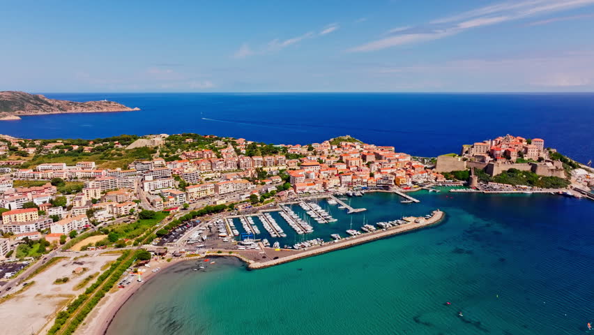 Aerial drone shot over the coastal town of Calvi in Corsica. View of the citadel fortress overlooking the city. Summer holidays destination. Bright blue sky, vibrant turquoise sea.