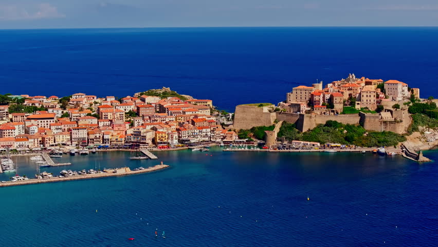 Aerial drone shot over the coastal town of Calvi in Corsica. View of the citadel fortress overlooking the city. Summer holidays destination. Bright blue sky, vibrant turquoise sea.