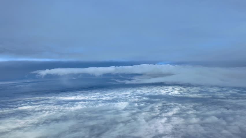 A pilot’s eye view while flying between endless layers fluffy clouds, while doing a right turn.