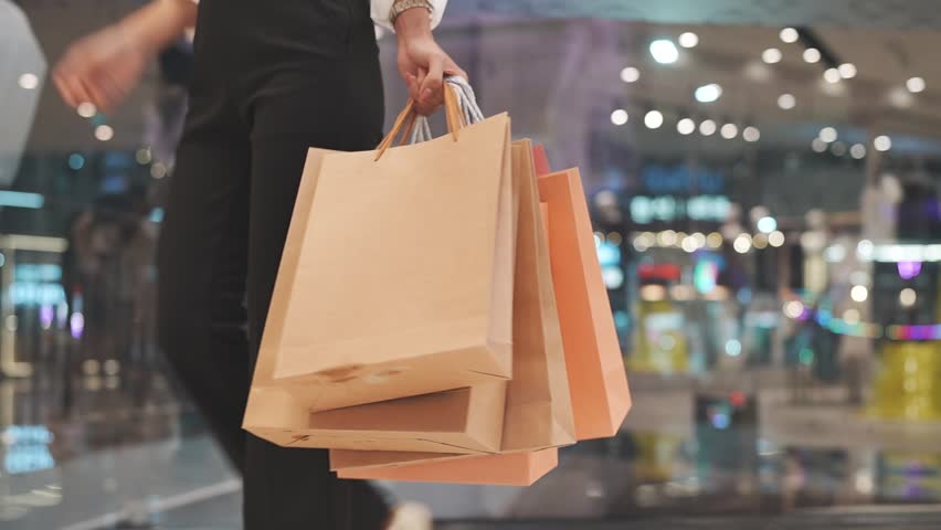 Close-up of a person holding multiple shopping bags in a mall, symbolizing retail therapy, consumerism, and modern lifestyle.