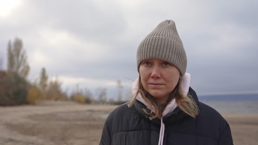 On a cool day by the lakeshore, a woman stands thoughtfully, taking in the peaceful surroundings. Soft clouds and gentle waves create a calming backdrop as she gazes towards the horizon.