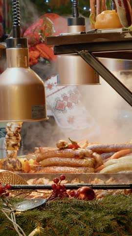 Vertical Screen Delicious meats and sausages are showcased at a festive market. The warm lights and seasonal atmosphere invite visitors to taste the holiday delights available.
