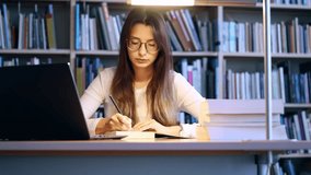 Student taking notes at library desk with laptop beside - Powered by Shutterstock - Get 15% off with code: PIKWIZARD15
