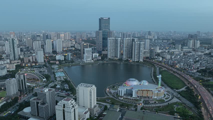 Hyperlapse dusk view of Hanoi skyline with dramatic clouds, golden sunlight, and reflective lake below.