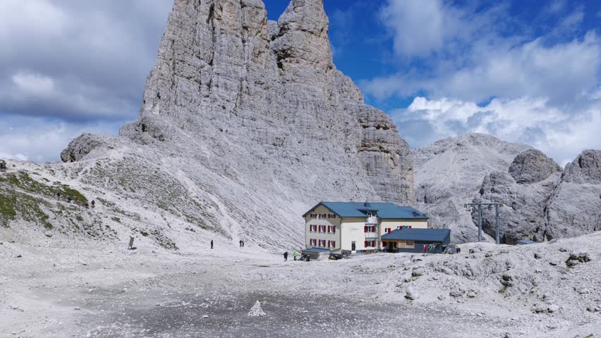 Stunning view of Vajolet Towers, Torri del Vajolet, and mountain refuge in Catinaccio group, hikers explore trails in iconic alpine landscape, Dolomites, Italy. Aerial backward