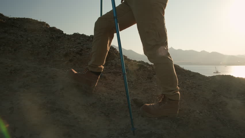 Hiker in hiking boots climbing up mountain ridge in sun lens flare at sunset, side view