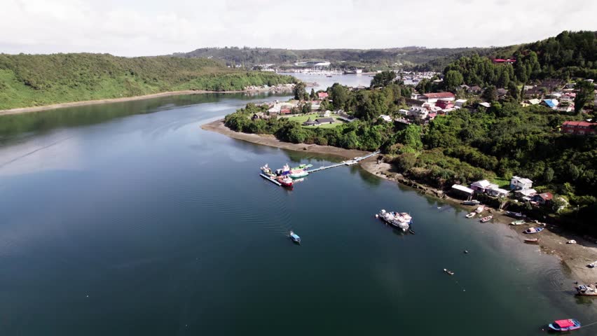An aerial view captures the port city of Puerto Montt, Chile, along the Pacific bay, with the dense urban development extending up the hillsides and the surrounding natural landscape visible