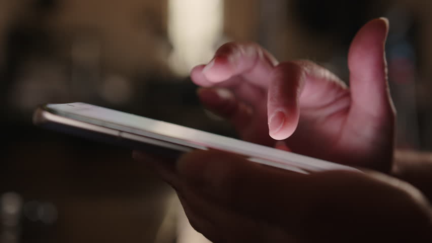 Woman hand using smartphone in room scrolling mobile phone touch screen with finger close up side view