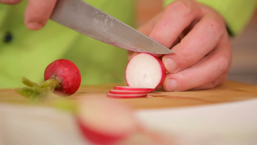 Chef is slicing radish with a knife on a cutting board