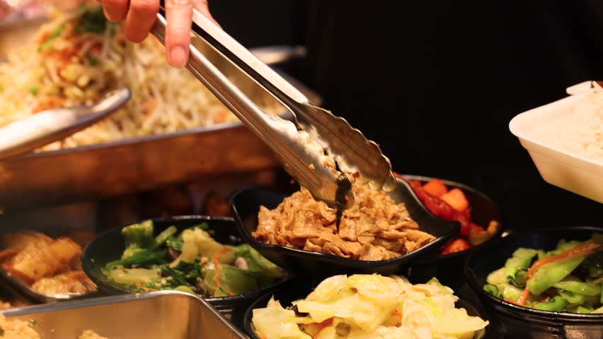 Vendor serving Asian cuisine into a white disposable polystyrene container at a busy food court, ready for takeout to work or home, illustrating fast casual dining and everyday urban