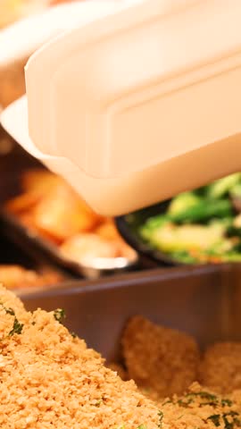 Close-up of tongs picking various Asian vegetable and meat dishes at a food court, placing them into disposable takeout containers, illustrating custom meal selection and convenient urban dining