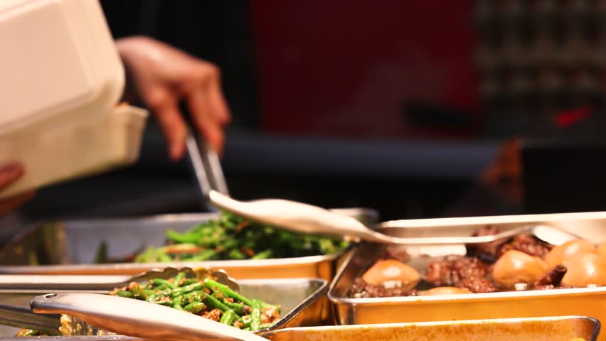 Wide selection of Asian cuisine including vegetables, fish, and meat dishes available at a busy food court, served into disposable containers for convenient takeout and urban dining