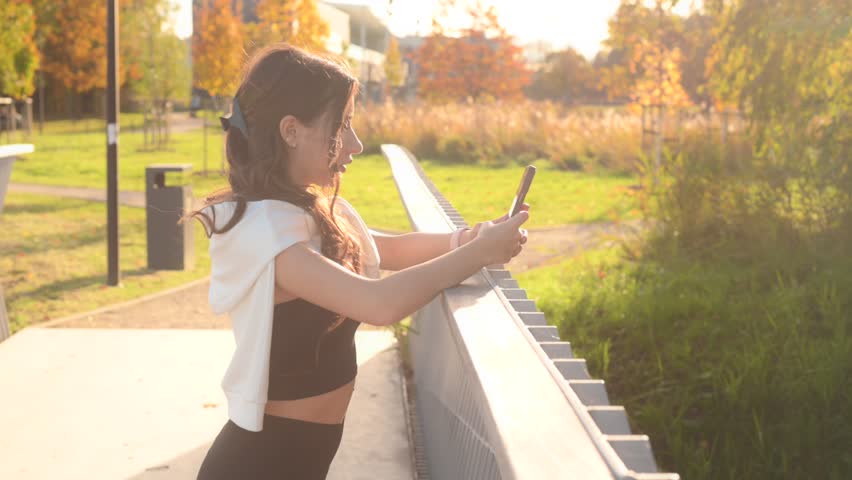 Young sporty woman in activewear using smartphone on a sunny autumn day after training outdoor