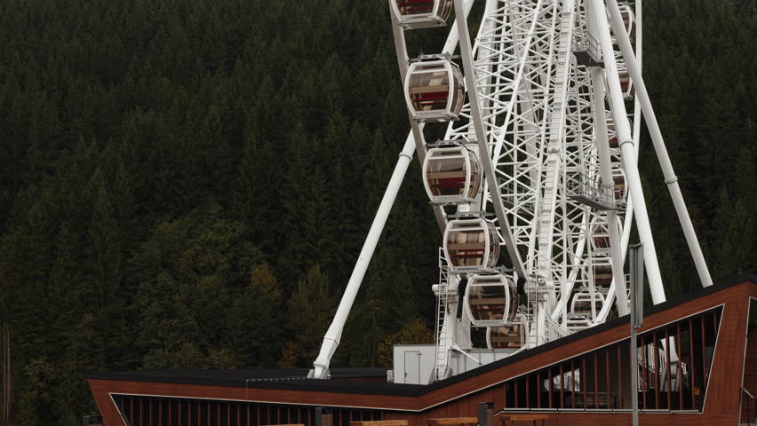 Modern Ferris wheel beside wooden building in forest resort
