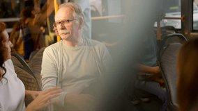 Mature man and woman engaged in a lively conversation while sitting on a city bus, commuting through the urban streets during their daily travel routine with other passengers in the background - Powered by Shutterstock - Get 15% off with code: PIKWIZARD15