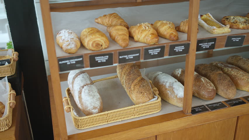Variety of fresh baked sourdough, seeded bread, croissants, danishes, and baguettes display on wooden shelf in bakery shop