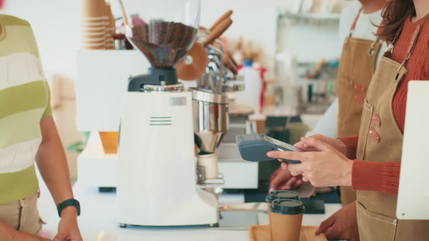Asian woman paying for purchase with smart watch at coffee shop. Contactless payment at cafe restaurant. Customer using NFC Smartwatch making payment, paying on terminal. Cashless payment technology.