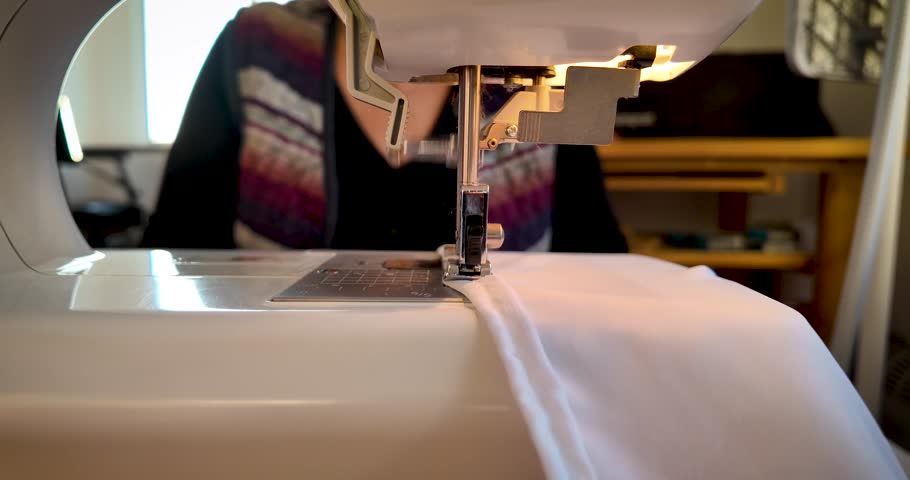 4K close-up footage of a sewing machine finishing white fabric, expertly guided by a woman’s hand. Perfect for fashion, craftsmanship, textile, and handmade production projects.