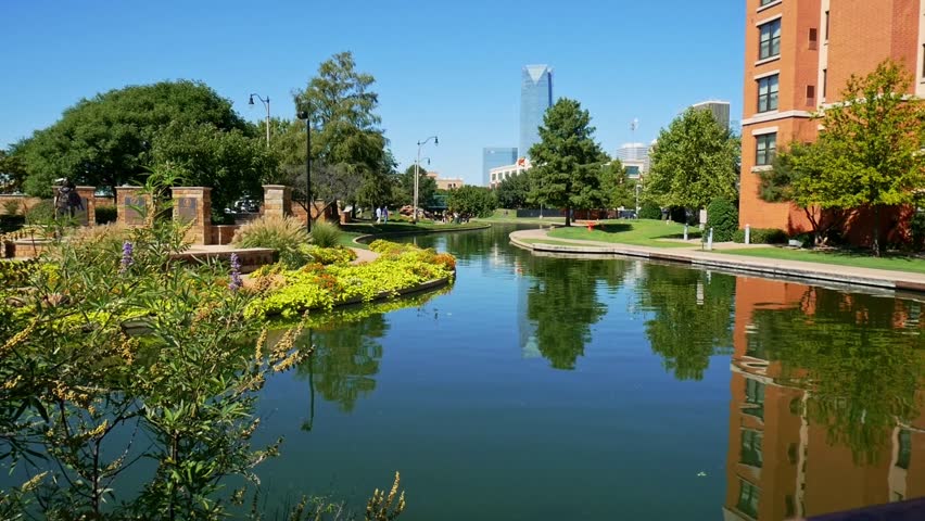 Steady left to right shot of Bricktown Canal in Oklahoma City with people walking, clear blue sky and Devon Tower Energy Center in the background
