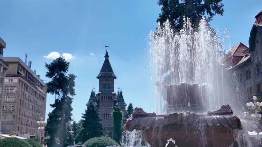 Scenic view highlighting the cathedral and active fountain in Timisoara, emphasizing architecture, water features, and urban charm.