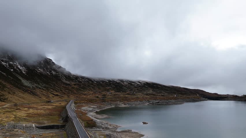 A breathtaking aerial view of a narrow road winding through a serene lake in the heart of the Alps at Splügen Pass italy