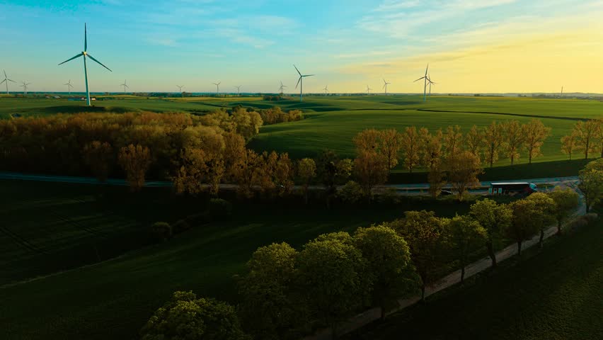 Road with driving cars close to wind generators farm spinning. Vehicles moving near wind turbine field rotating in breeze. Automobiles traveling along route beside renewable energy landscape